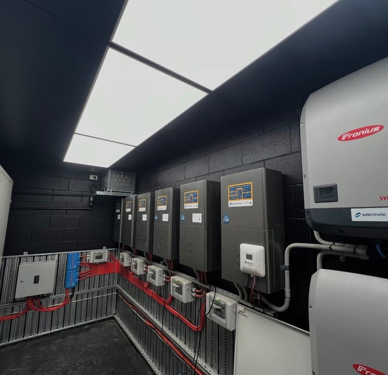 Industrial electrical equipment room with large metal panels, white machinery units, and red safety barriers along the floor